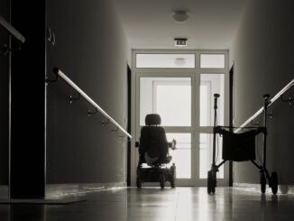einsamer Korridor mit Gehhilfe und Elektro-Rollstuhl vor einer Glastür, in einem Pflegeheim.